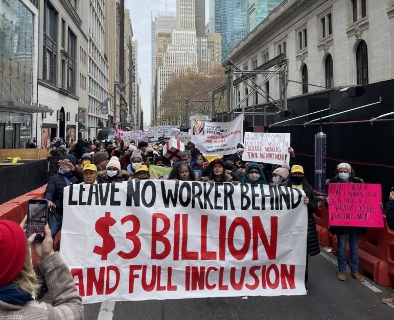 Gente marchando con un letrero que dice "No deje a ningún trabajador atrás. $3 mil millones financian la inclusión total"