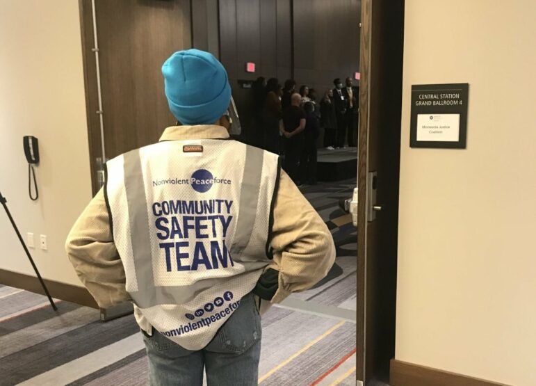 Mujer con chaleco del Equipo de Seguridad Comunitaria fuera de la sala de conferencias