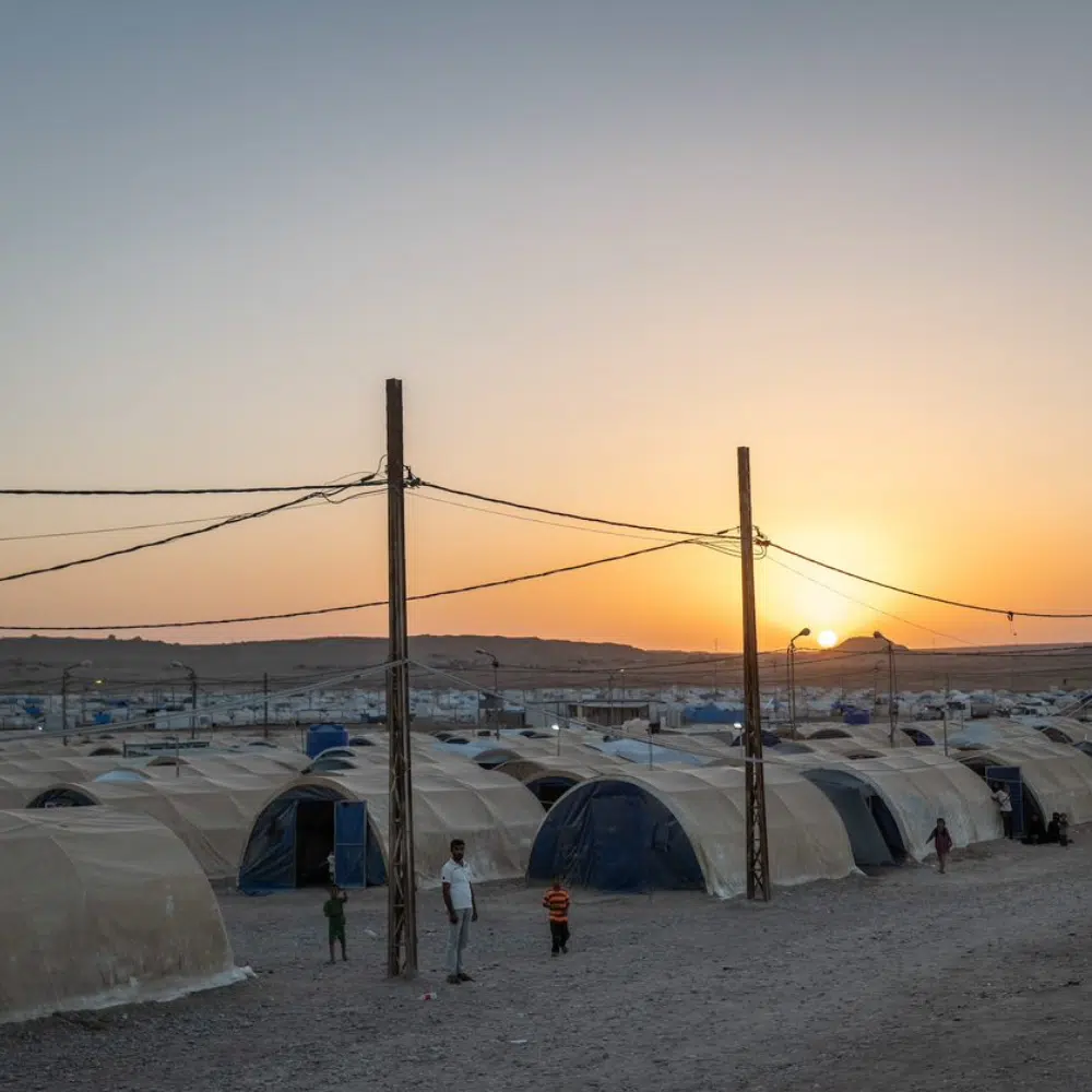 Coucher du soleil par des tentes et des poteaux électriques le long d'un chemin de terre.