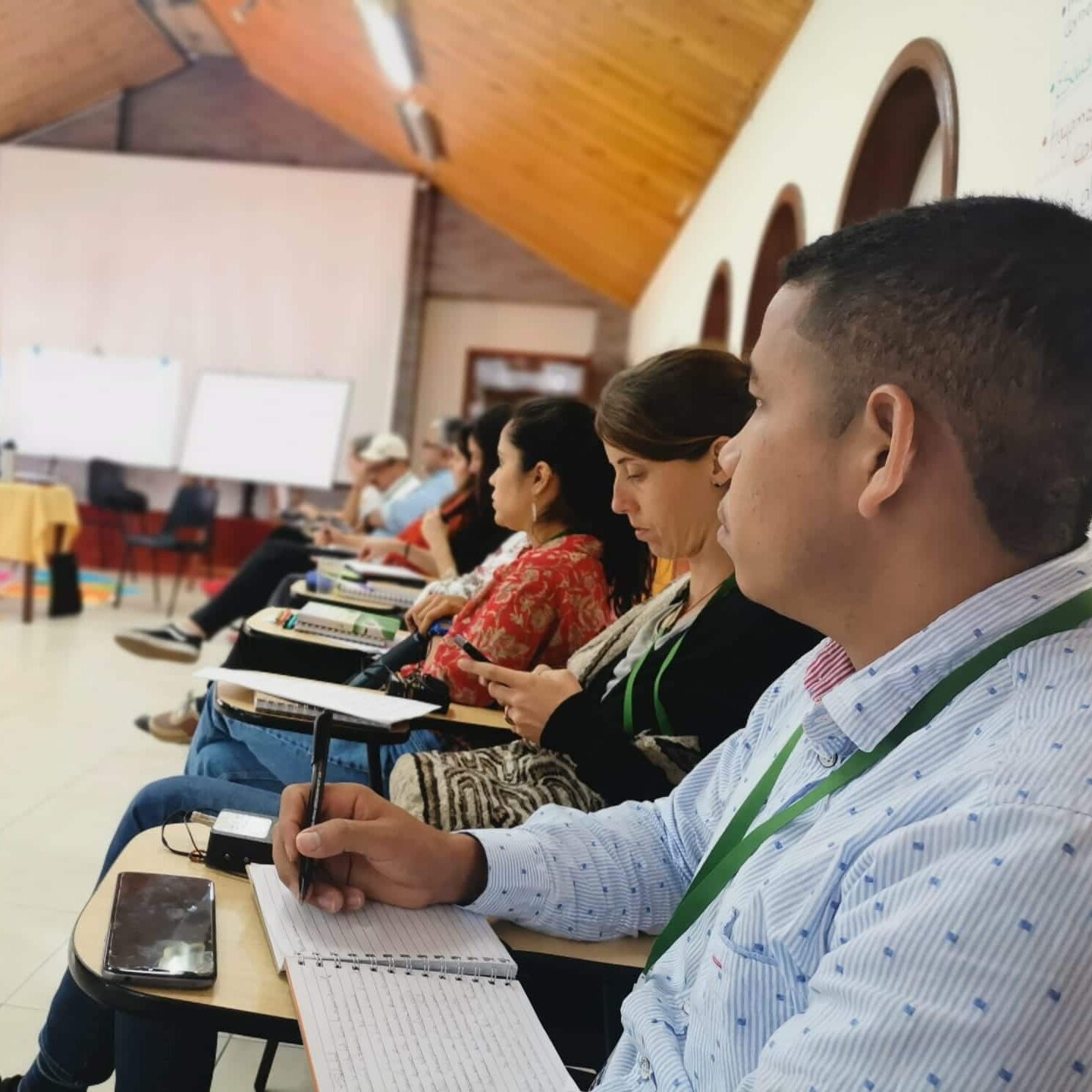 A group of inviduals take notes while they sit in a circle of chairs for a workshop.