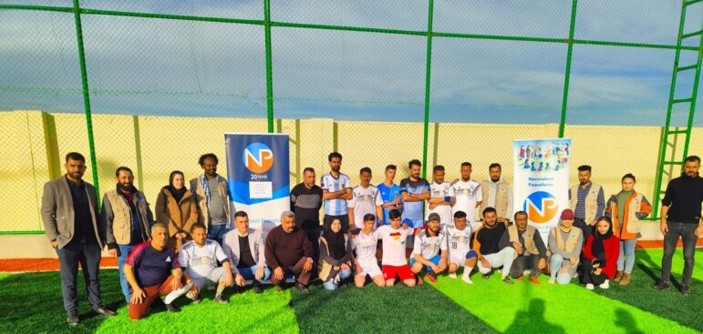 NP staff take a group photo with football players from the youth peace team in Ba'aj, Iraq. The turf is two shades of green.