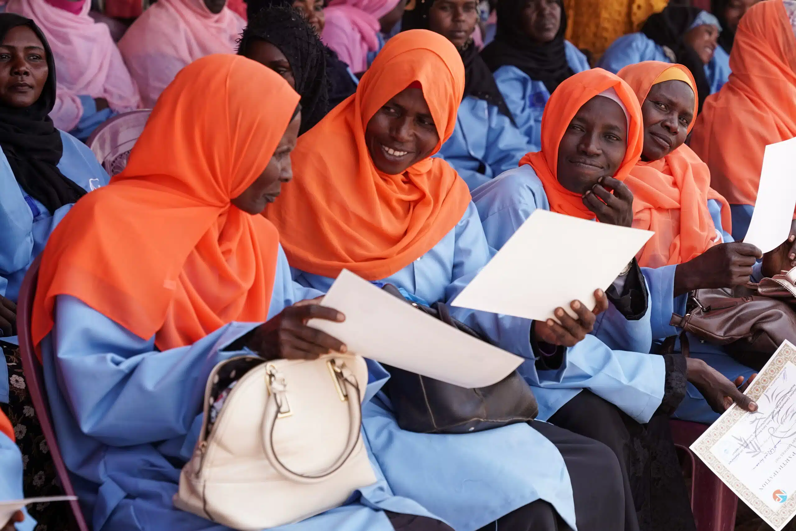 Varias mujeres sudanesas con pañuelos en la cabeza sentadas en filas, sosteniendo certificados de reconocimiento.