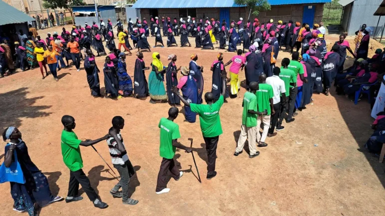 A group of individuals gathered in an open space, some holding what appear to be sticks and others wearing colorful clothing.
