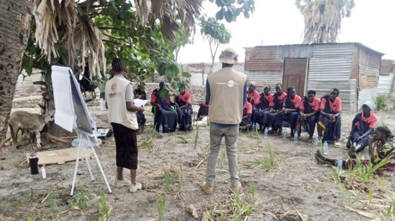 A Nonviolent Peaceforce staff member and Solidarites International staff member are standing outdoors while presenting on WASH awareness to  the Meer- Women Civic Action Group in Warjwok, Malakal, Upper Nile. 