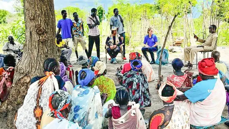 A group of community members, mostly women are sitting on the ground outdoors as they speak with Nonviolent Peaceforce staff, Solidarites International staff, and European Union representative, Alice Vantournhoudt. Location is Malakal, Upper Nile, South Sudan. 
