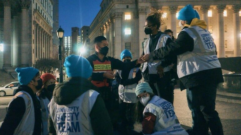 Nonviolent Peaceforce staff and volunteers during an action -- they are wearing blue NP beanies, white Community Safety Team vests, layers for the cold New York, and face masks