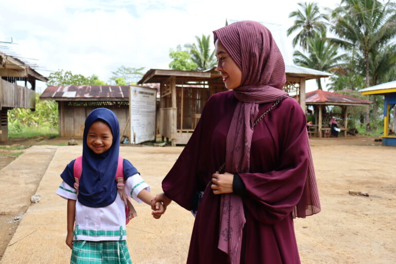 Najah takes the hand of a young student as she walks with her to her classroom.