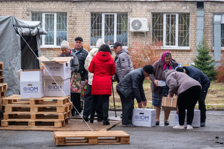 Розподіл гуманітарної допомоги. Харків, 2024. Гуманітарні працівники пропонують українським цивільним особам коробки з предметами взаємодопомоги. На коробках є логотип МОМ ООН з питань міграції. ©NP