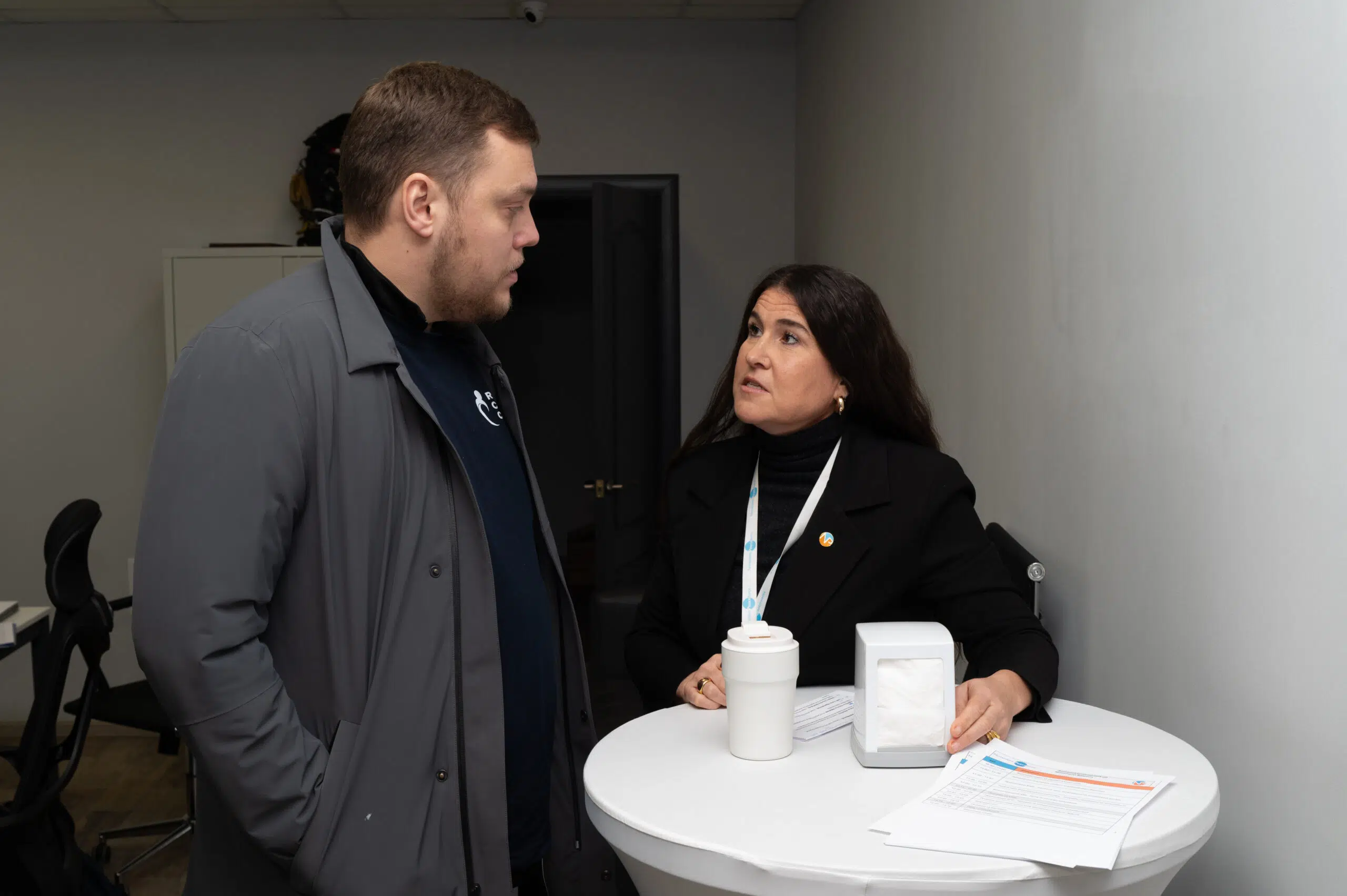 NP Ukraine staff works with local community partners. Two people are standing while working at a tall white table and mid-discussion.