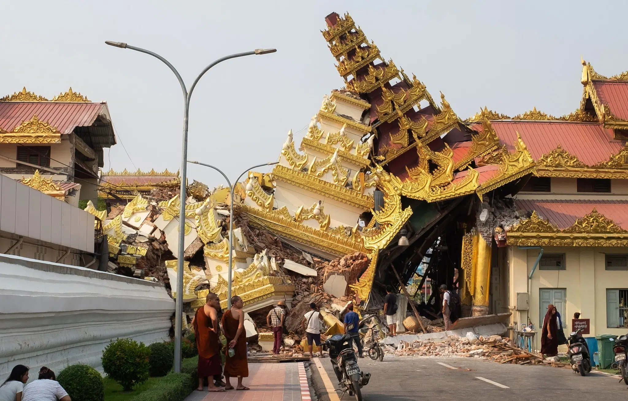 Several civilians stand near the collapsed remains of the Maha Myat Muni Buddhist pagoda in Mandalay, observing the rubble left by an earthquake.