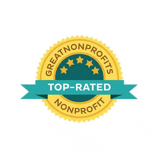 A gold badge with five stars and the words GreatNonprofits Top-Rated Nonprofit in bold letters. A teal ribbon labeled Top-Rated runs across the center of the badge. The background is white.