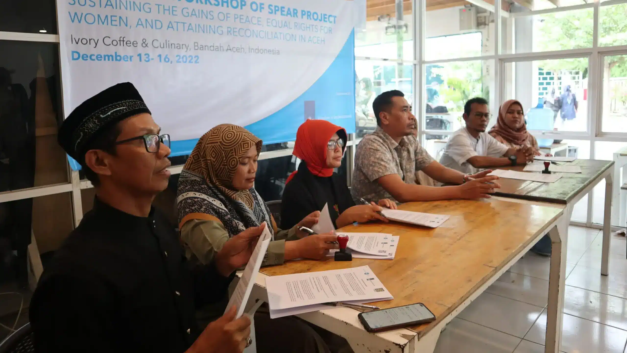 A group of individuals sit at a table in front of sign that reads, " Inception Workshop of SPEAR Project | Sustaining the Gains of Peace, Equal Rights for Women, and Attaining Reconciliation on Aceh"