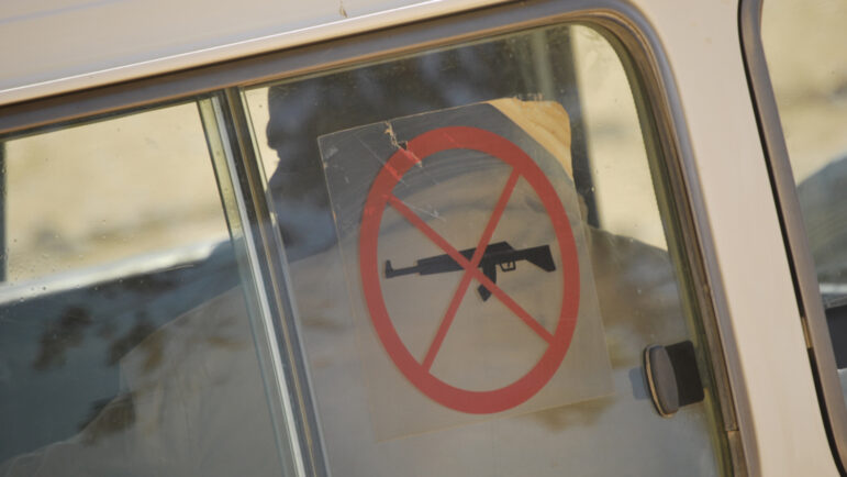 window of a vehicle. transparent sticker has a image of a gun with a red circle and X around it, indicating no guns or weapons.